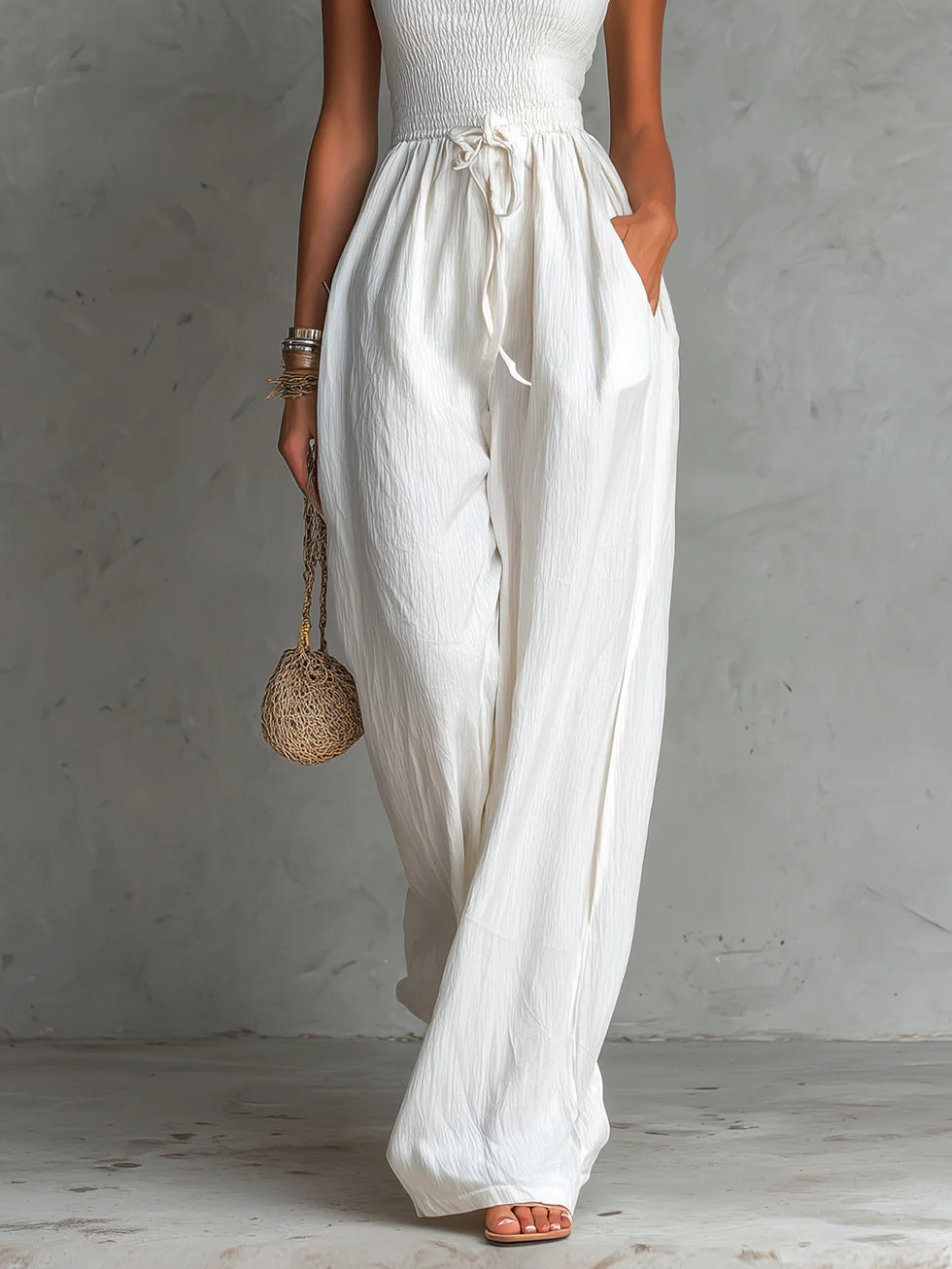 White sleeveless jumpsuit with a square neck, pleats, adjustable drawstring, and wide leg